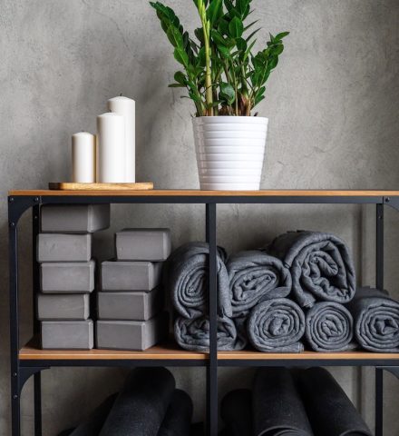 the interior of the room is a studio for sports yoga or stretching. table rack with accessories for classes – gray support cubes, rubber mats and plaids. decor candles and zamioculcas zamiifolia plant Yoga